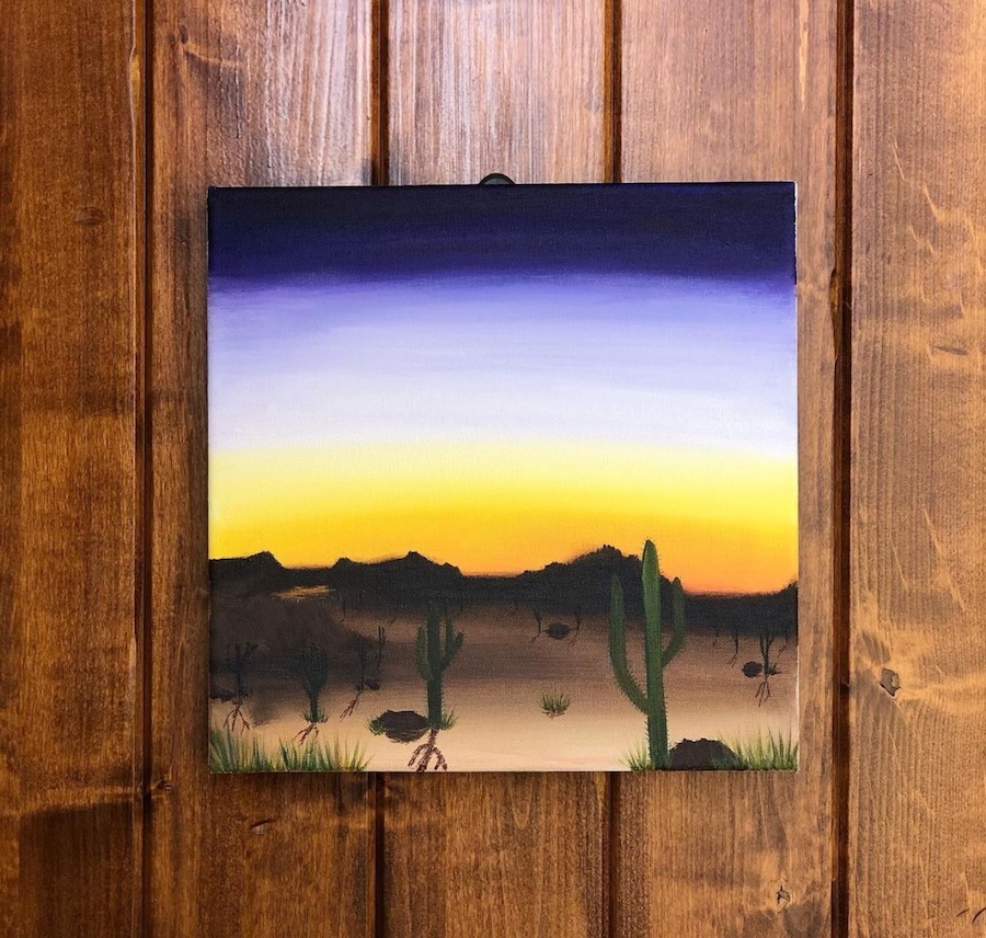 A landscape painting of the Arizona desert with the sun setting behind the mountains.